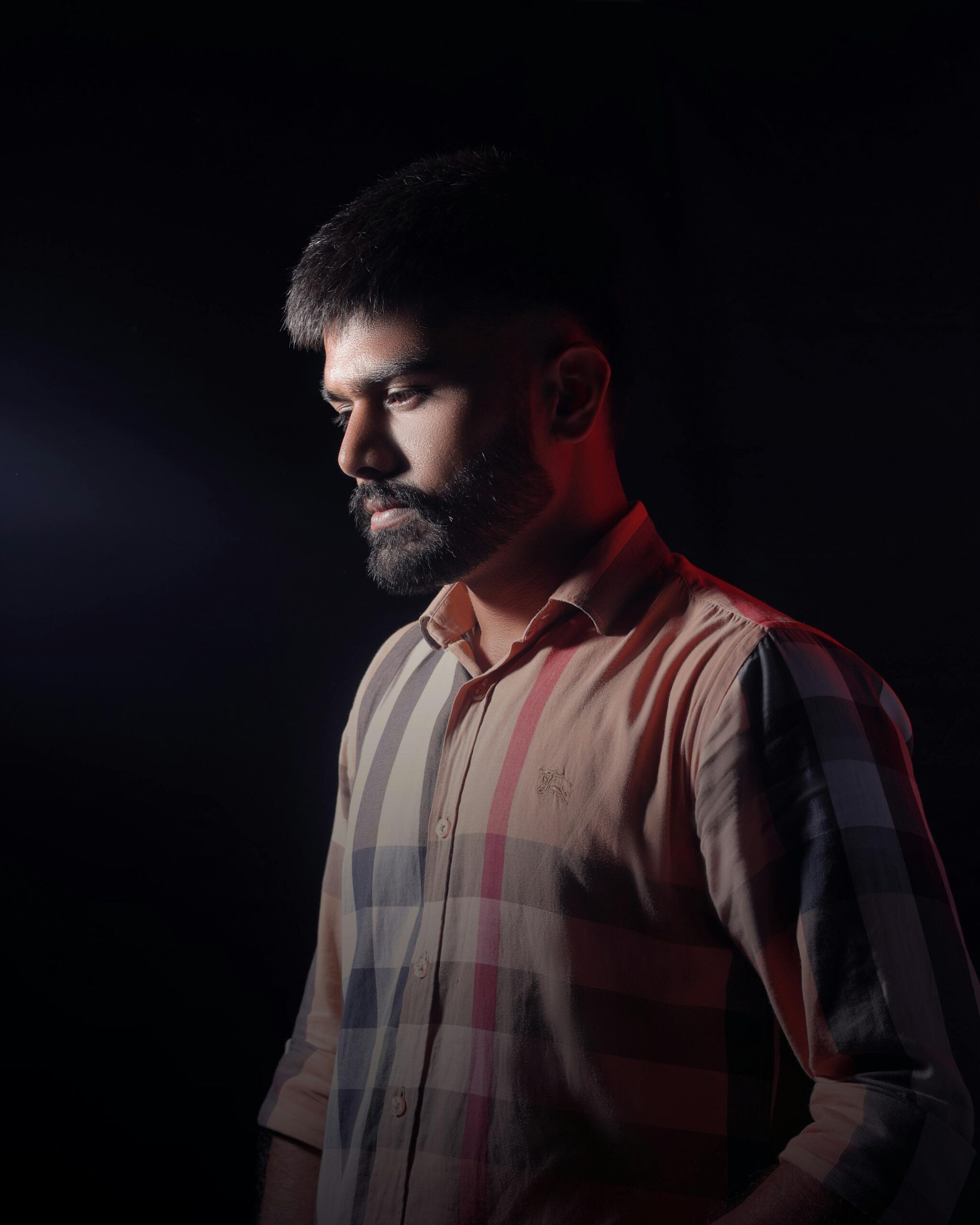 Moody portrait of a bearded man in warm lighting, wearing a plaid shirt, against a dark background.
